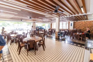 Sabah seafood restaurant showcasing wooden beam ceiling design, circular dining tables with brown chairs, geometric tile flooring, and abundant natural light for a welcoming dining ambiance