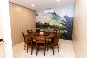 Private dining room with round wooden table and chairs featuring tropical landscape mural wall art, light wood paneling, and air conditioning for comfortable dining experience.
